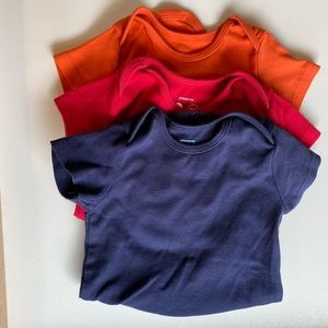 Four Primary signature short sleeve baby suits in Cherry, Orange, and Navy.